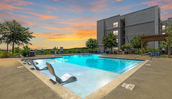 A large swimming pool with lounge chairs and a building in the background.