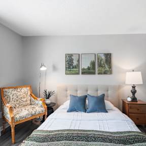 A bedroom with a bed, chair, and two pictures on the wall.