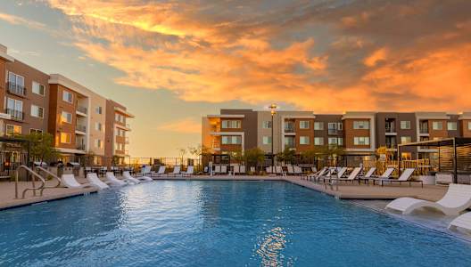 a swimming pool at sunset with an apartment building in the background
