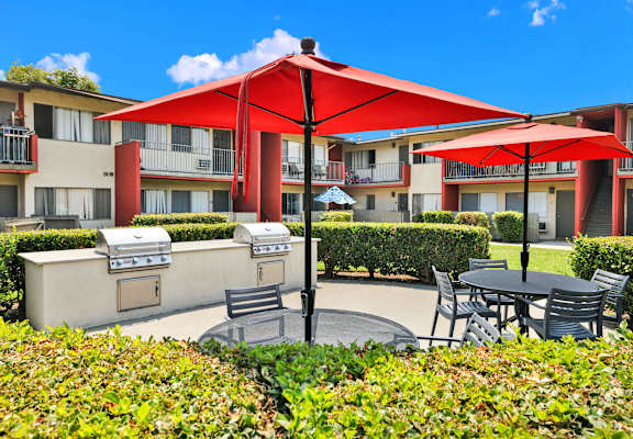 a patio with tables and umbrellas in front of an apartment building