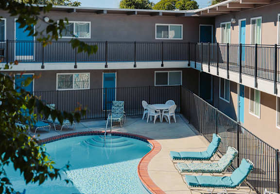 A pool with a table and chairs is surrounded by a black fence.