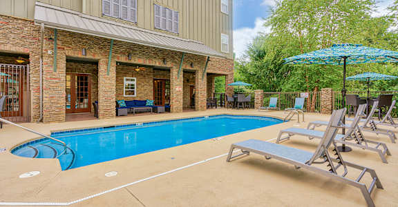 A pool area with sun loungers and a building in the background. at The Lofts at Reynolds Village Apartments, Asheville