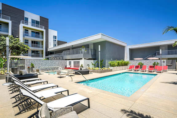 A pool area with sun loungers and a building in the background.