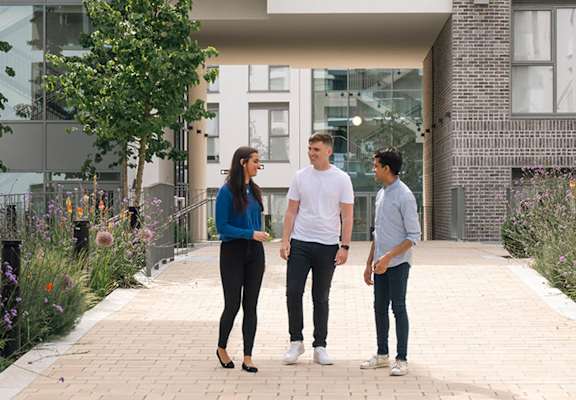 Three people are standing on a pathway between buildings.