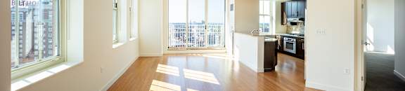 A large open living room with wooden floors and a balcony with a view of the city at Residences Providence, Providence, Rhode Island