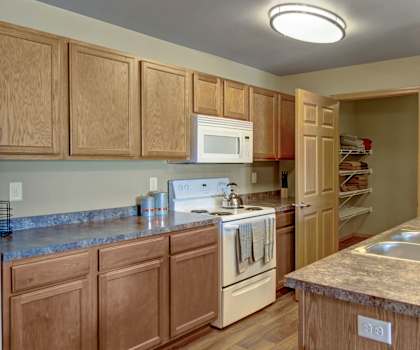 A spacious kitchen with white appliances, overhead lighting, light granite counter, and large light wooden cabinets at Vue 28 Apartment Homes. 
