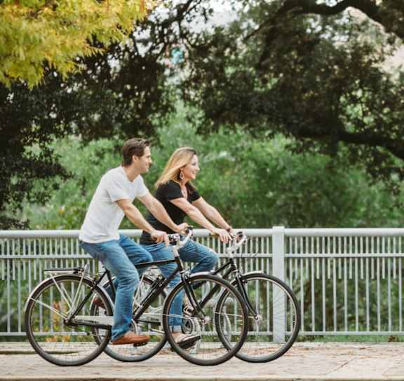 A man and a woman are riding a bicycle together at Arise Riverside Apartments, Austin, TX, 78741