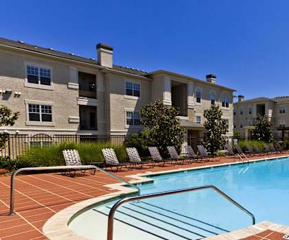 A swimming pool in front of a building with a fence and trees.