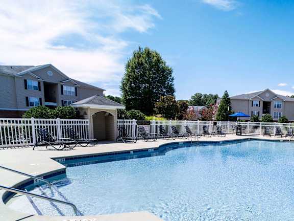 A swimming pool surrounded by a white fence and lounge chairs.