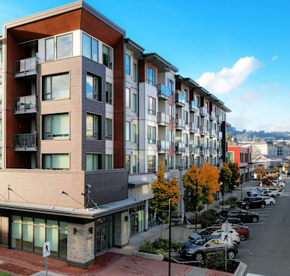 A modern multi-story apartment building with a parking lot in front.