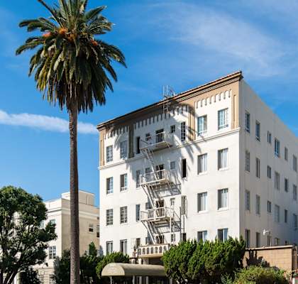 A white building with a balcony is surrounded by palm trees.