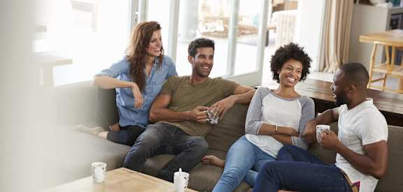 Lifestyle photo of a group of four friends sitting on a couch drinking coffee