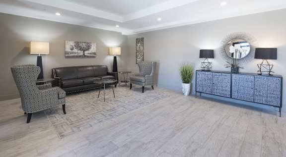 A well-lit living room with a grey sofa, a grey armchair, a grey side table, and a wooden floor.