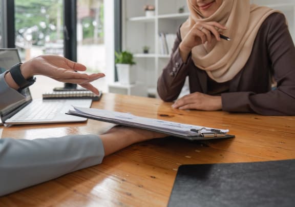 a woman sitting at a table with a man and a womanputing on a clipboard
