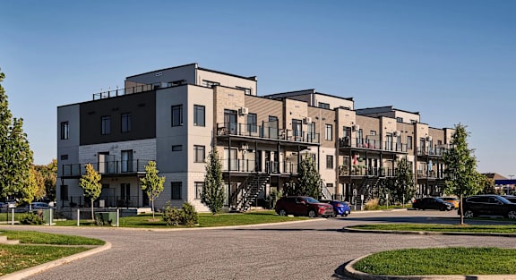 A row of modern townhouses with cars parked in front.