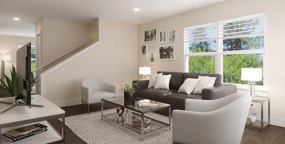 A modern living room with a grey sofa, a glass coffee table, and a staircase.