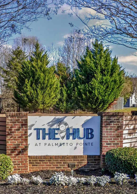 The sign for The Hub at Palmetto Pointe is surrounded by trees and shrubs.