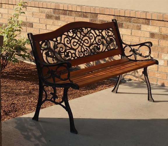 a wood and wrought iron park bench sitting in front of a brick wall
