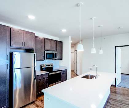 A spacious, modern kitchen with stainless steel appliances, overhead lighting, light countertops with lots of room, and large, dark wooden cabinets at Van Buren East Apartment Homes
