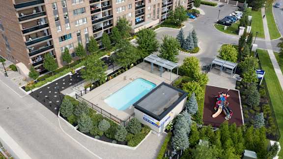 an aerial view of a swimming pool in the middle of a parking lot with trees