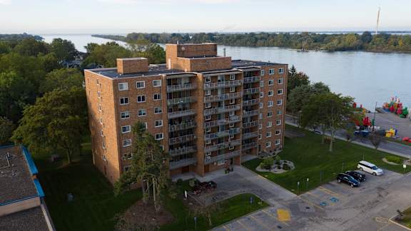A large apartment building sits on a grassy lot next to a body of water.