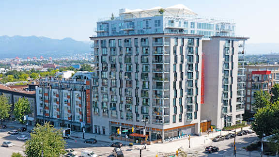 A large building with a red stripe on the side is in the foreground of a city street.