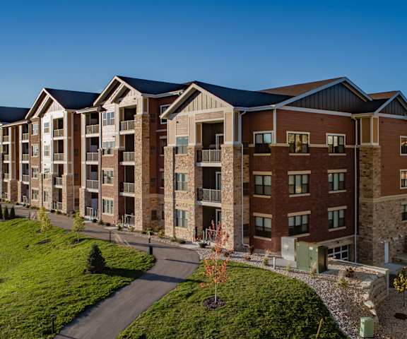 The stunning pathways surrounded by grass and trees leading to the brick apartment building at the Park Apartment Homes. 