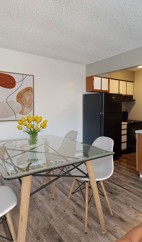 A dining room with a glass table, chairs, and a vase of flowers.