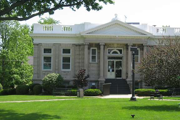 A large, stately building with a white roof and columns sits in a lush green park.