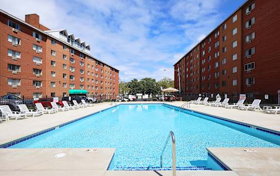 A large swimming pool surrounded by red brick buildings and lounge chairs.
