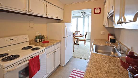 A kitchen with white appliances and a red towel on the stove.