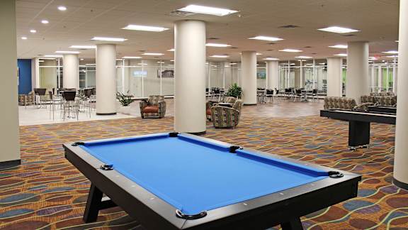 A pool table in the middle of a room with chairs and tables.