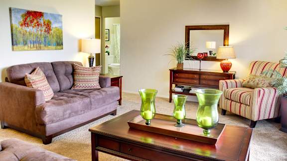 A living room with a grey couch, a coffee table with green vases, and a painting on the wall.