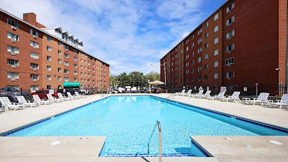 A large swimming pool surrounded by red brick buildings and lounge chairs.