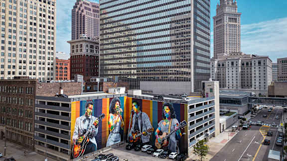 A large mural of three musicians is displayed on a building in a city.