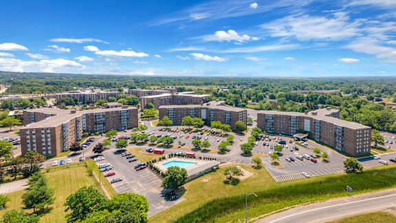 A large apartment complex with a parking lot and a pool.