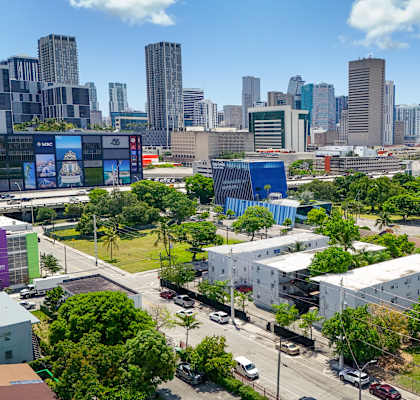 A cityscape with a mix of modern and older buildings, surrounded by greenery and a clear sky.