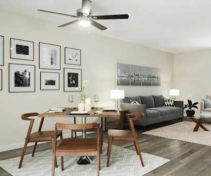 A living room with a grey couch, a wooden table and chairs, a rug, and a ceiling fan.