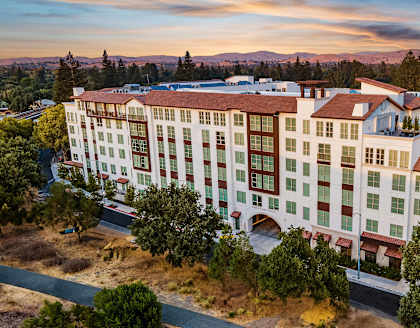 Sunset view of a Mediterranean-style apartment residence surrounded by rolling hills and natural beauty