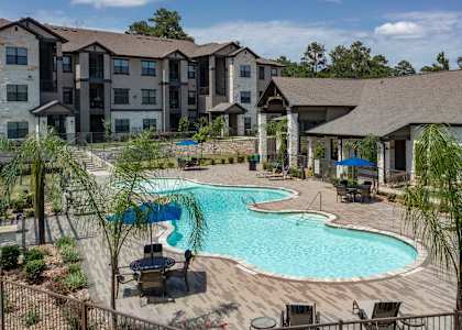 A large outdoor swimming pool surrounded by lounge chairs and trees.
