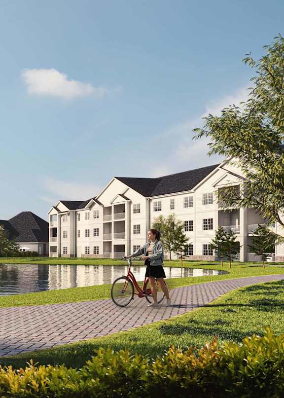 Exterior view of Lakeview Terrace apartments in Ridgeland, SC featuring modern architecture, landscaped walkways, and a resident walking a bike through the community.