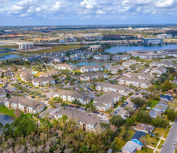 A bird's eye view of a residential area with houses, a lake, and a bridge in the distance. at The Villages on Millenia Apartments, Orlando, FL, 32839