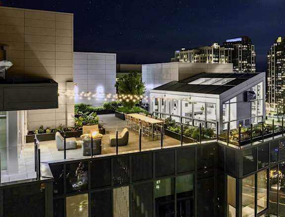 A modern building with a rooftop garden is illuminated at night.