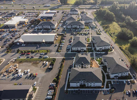 A large white building with a black roof is surrounded by a parking lot.