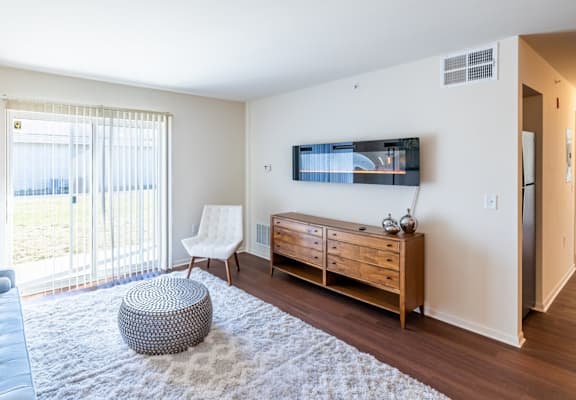 A living room with a blue couch, a white chair, a wooden cabinet, and a flat-screen TV mounted on the wall.