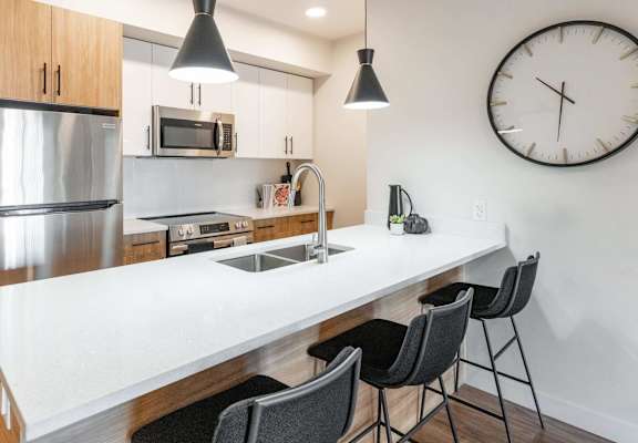 A modern kitchen with a white countertop and black chairs. at Cadence at Griesbach, Edmonton, AB