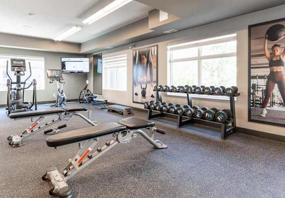 A spacious gym with a variety of equipment and a large poster of a woman exercising. at Cadence at Griesbach, Edmonton, AB