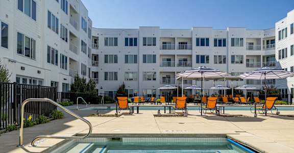 a pool with yellow chairs and umbrellas in front of an apartment building