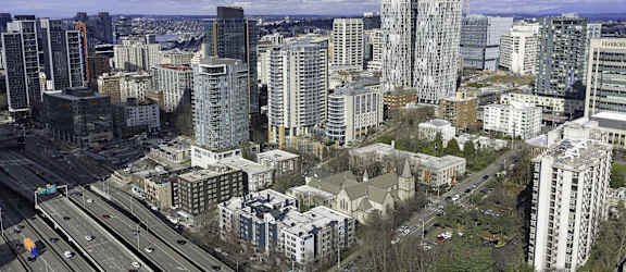 A cityscape with a mix of modern and older buildings, a highway, and a cloudy sky.