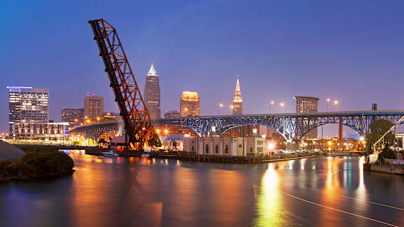 A bridge has collapsed over a body of water with a city skyline in the background.